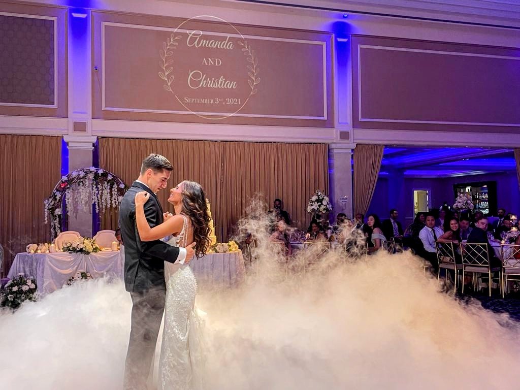 Couple dancing on clouds beneath a projected monogram